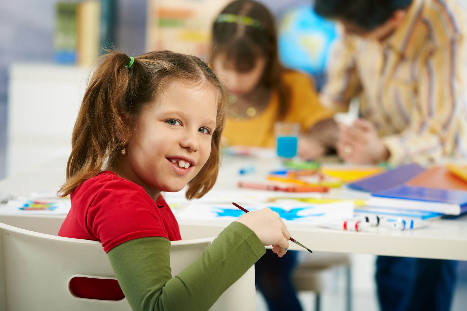 2 Kinder und 1 Betreuerin beim Malen von Bildern an einem Tisch