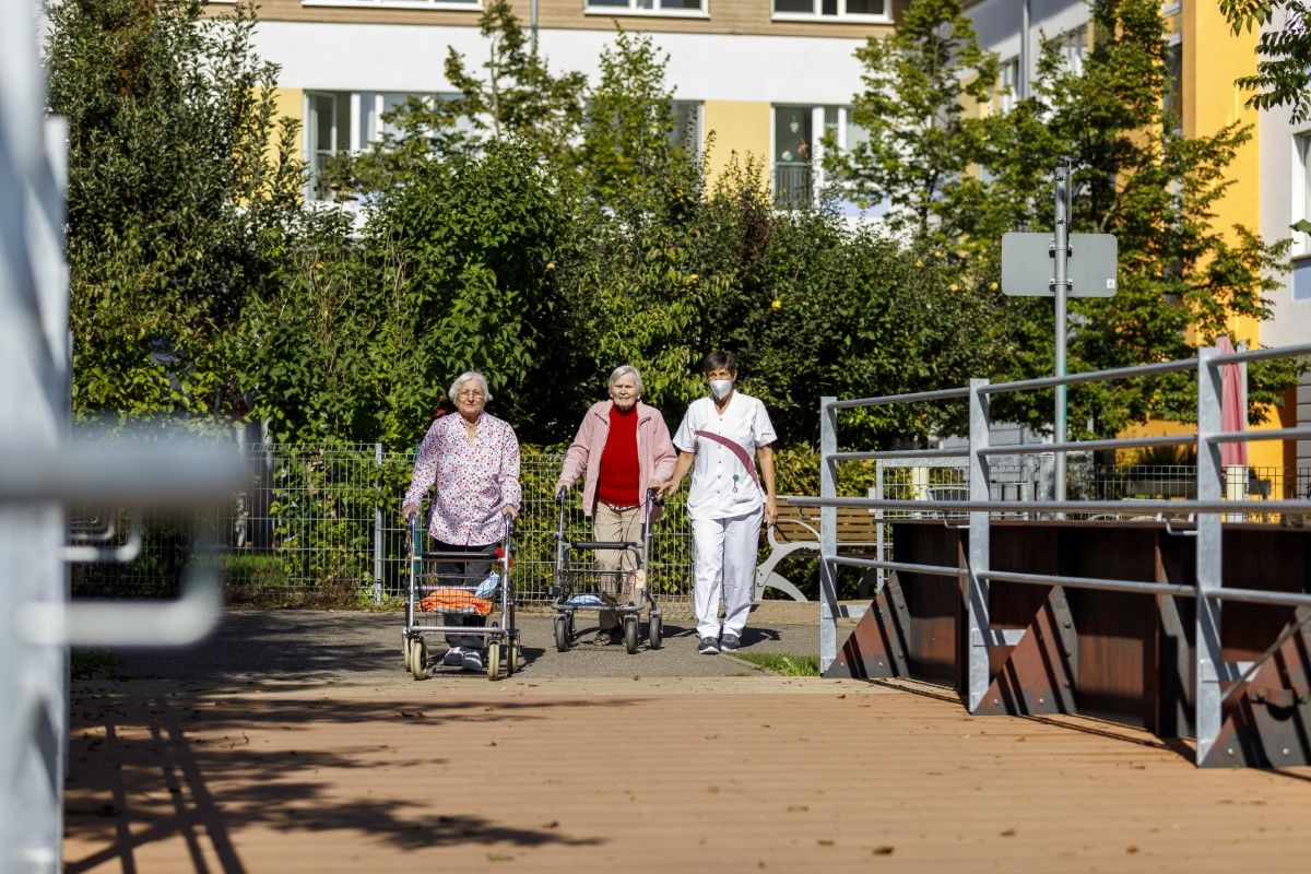 Zwei Bewohnerinnen gehen mit Pfleger spazieren